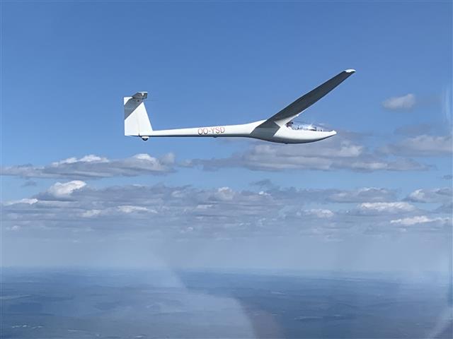 Photo d'un planeur en vol sous un ciel nuageux et soleil couchant.